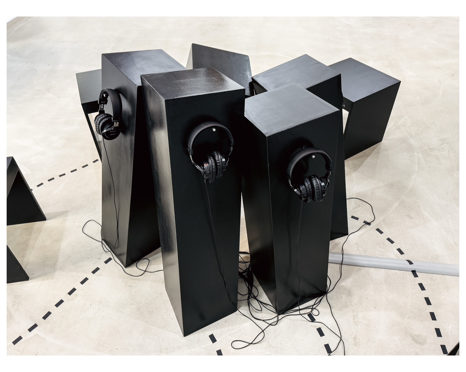 Detail of the central structure: black beams leaning into one another for support, each carrying a pair of headphones.
