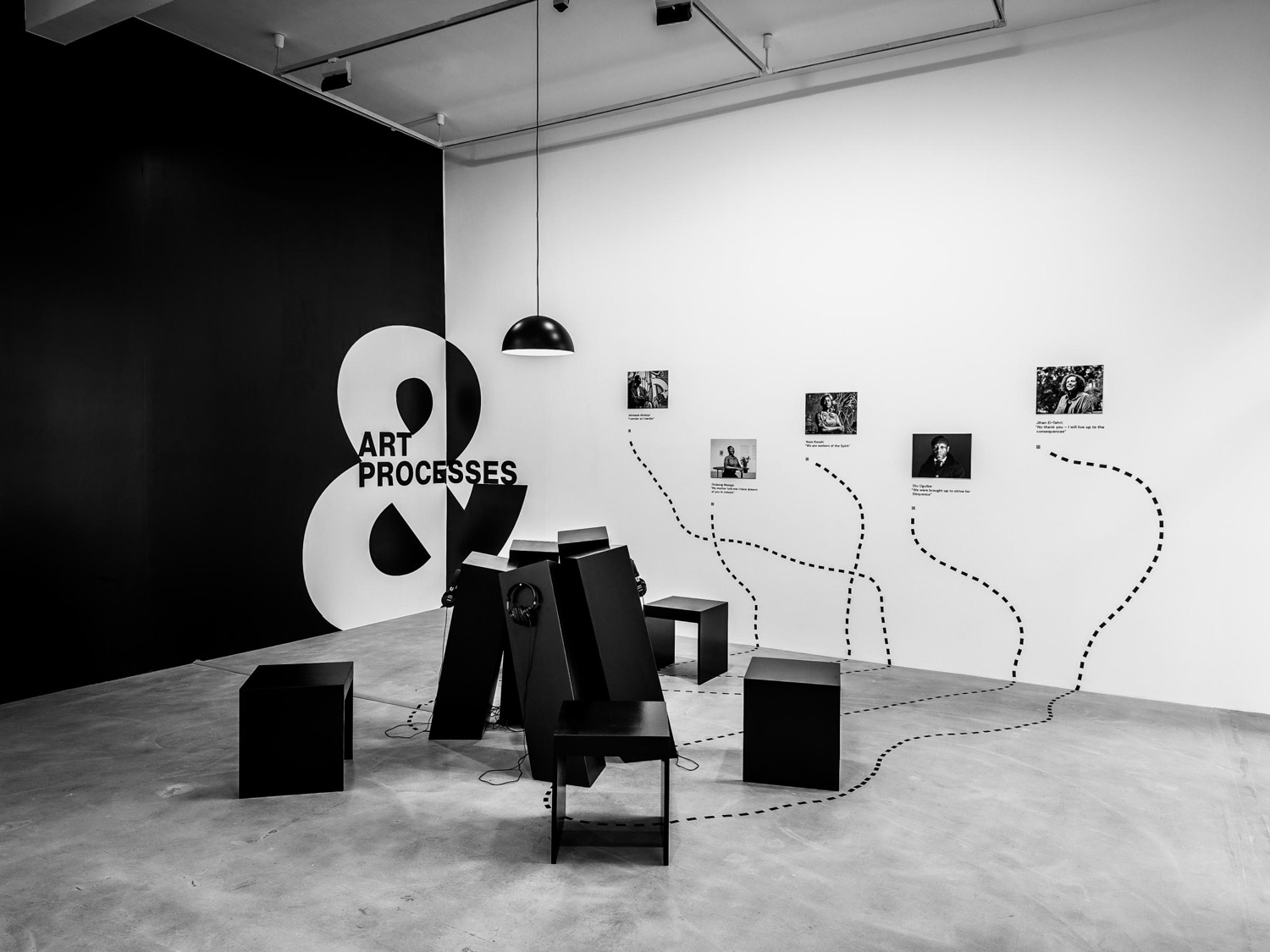 Gallery installation: dark listening stations on a pale floor, framed images on the wall linked by a dotted line.
